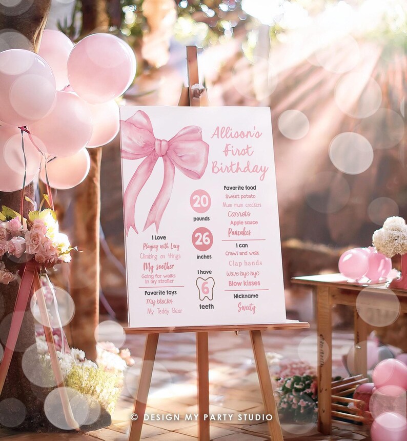 May include: A pink and white first birthday sign with a large pink bow at the top. The sign lists the child's age, weight, height, favorite foods, and activities. The text on the sign reads "Allison's First Birthday".