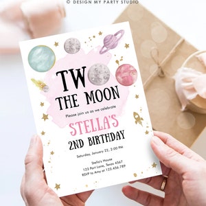 May include: A pink and white invitation with gold stars and planets. The text reads "Two the Moon, Please join us as we celebrate Stella's 2nd Birthday, Saturday, January 22, 2:00 PM, Stella's House, 123 Part Lane, Texas 4567, RSVP to Amy at 123.456.789".
