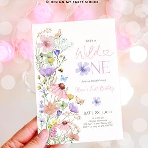 May include: A floral-themed first birthday invitation with a watercolor design featuring pink, purple, and yellow flowers, butterflies, and a bee. The text reads "She's a Wild One" and includes details for the party, including the date, time, location, and RSVP information.