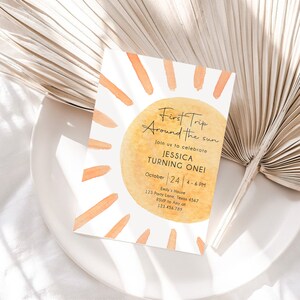 Peut inclure: Une illustration aquarelle d'un soleil avec le texte "First Trip Around the Sun" et "Join us to celebrate Jessica Turning One!" L'invitation comprend &eacute;galement la date "October 24", l'heure "4-6 PM" et l'adresse "Emily's House, 123 Party Lane, Texas 4567".