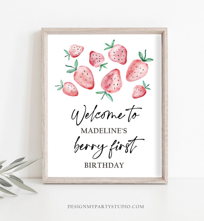 May include: A white sign with a wood frame and a watercolor illustration of strawberries. The sign says "Welcome to Madeline's berry first birthday".