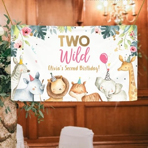 May include: A white banner with the text "TWO Wild Olivia's Second Birthday!" in gold and pink lettering. The banner features a jungle theme with illustrations of a zebra, rhinoceros, lion, tiger, elephant, and giraffe wearing party hats.