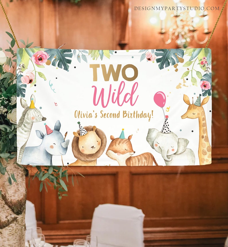 May include: A white banner with the text "TWO Wild Olivia's Second Birthday!" in gold and pink lettering. The banner features a jungle theme with illustrations of a zebra, rhinoceros, lion, tiger, elephant, and giraffe wearing party hats.