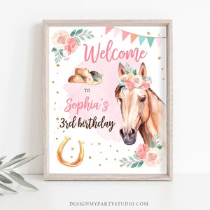 May include: A pink and white welcome sign with a watercolor illustration of a horse wearing a floral crown. The sign says "Welcome to Sophia's 3rd birthday" with a gold horseshoe.
