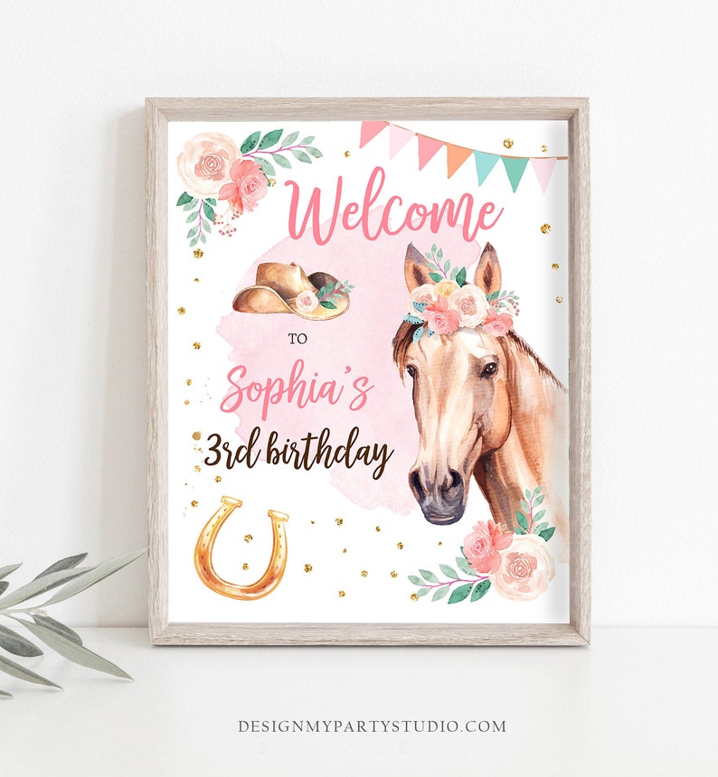 May include: A pink and white welcome sign with a watercolor illustration of a horse wearing a floral crown. The sign says "Welcome to Sophia's 3rd birthday" with a gold horseshoe.