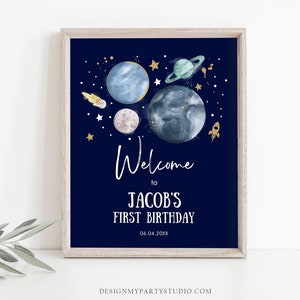 May include: A navy blue welcome sign with a space theme. It features planets, stars, and a rocket ship. The text reads "Welcome to Jacob's First Birthday 06.04.20XX".