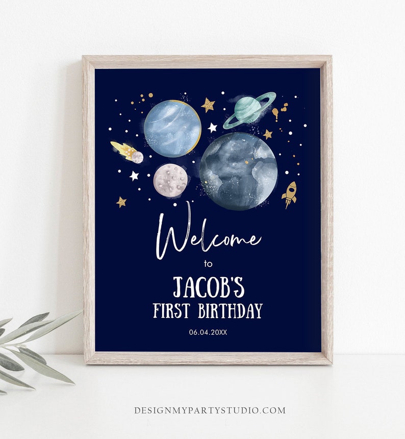 May include: A navy blue welcome sign with a space theme. It features planets, stars, and a rocket ship. The text reads "Welcome to Jacob's First Birthday 06.04.20XX".