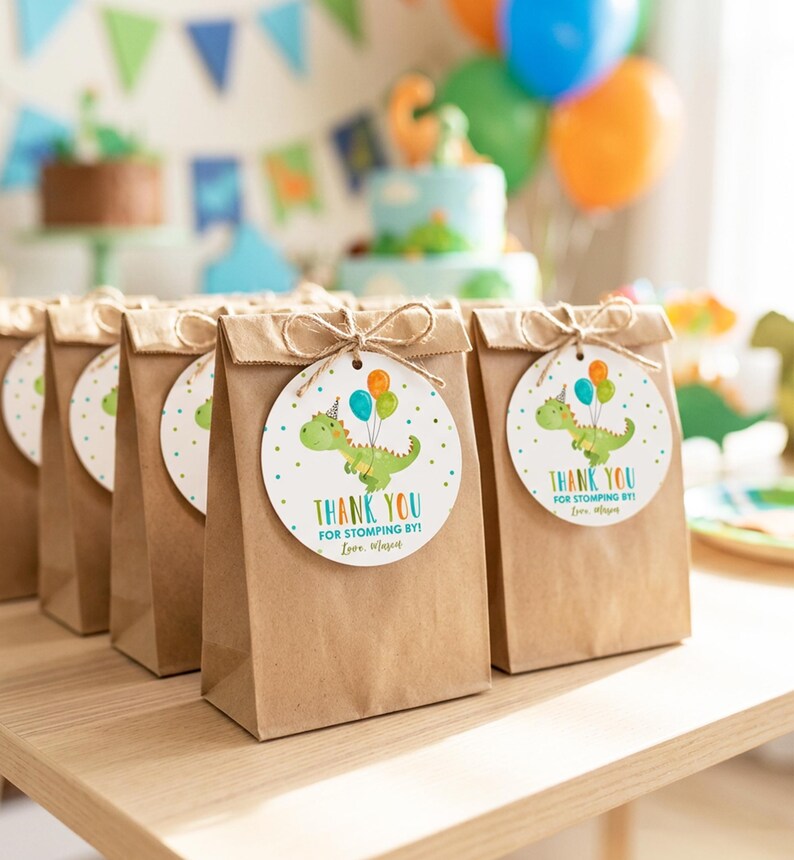 May include: A row of brown paper gift bags, each featuring a round white tag tied with twine. The tag displays a green cartoon dinosaur wearing a party hat, holding three colorful balloons, with the text Thank You For Stomping By! Love, Mason.