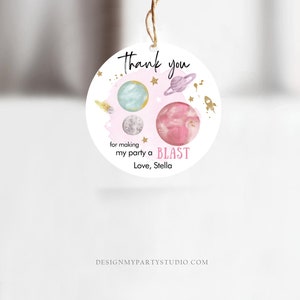 May include: Round pink and white thank you tag with a space theme. It features planets, stars, and a rocket ship. The text reads "Thank you for making my party a BLAST Love, Stella".