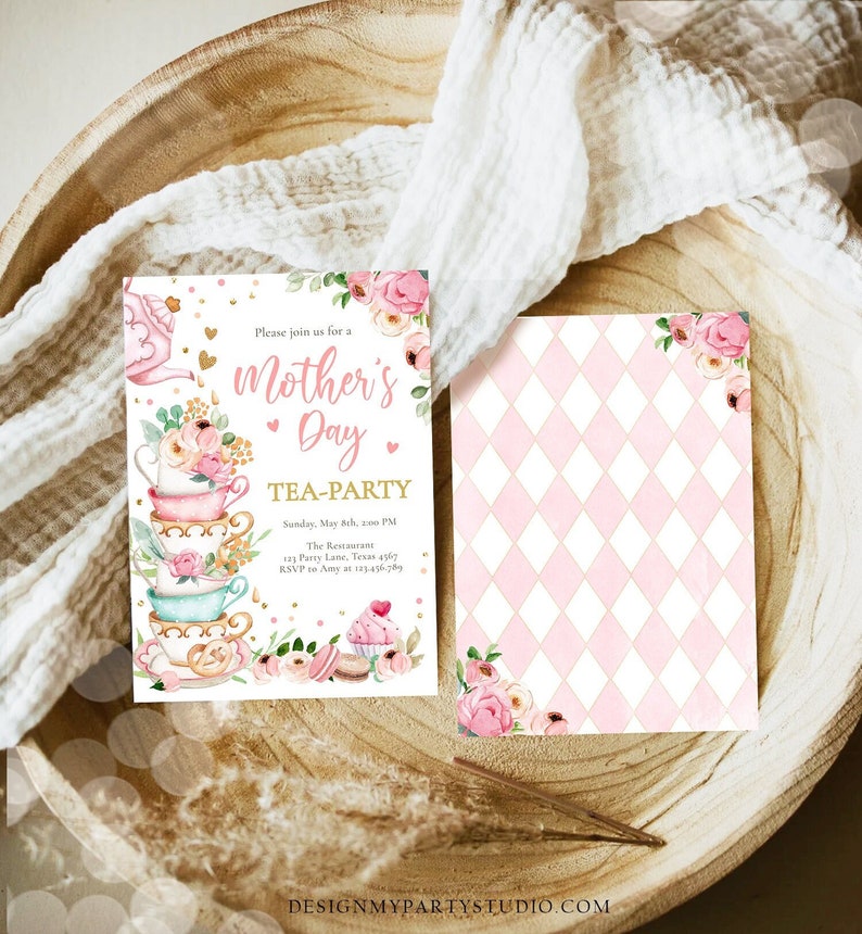 K&ouml;nnte beinhalten: Einladungen zur Teeparty zum Muttertag. Die Vorderseite zeigt einen Stapel Teetassen mit Blumengestecken und dem Text "Mother's Day Tea-Party". Die R&uuml;ckseite hat ein rosa-wei&szlig;es Rautenmuster mit floralen Akzenten. Die Einladungen liegen auf einem Holztablett.
