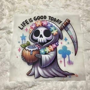 Puede incluir: Una imagen de dibujos animados de la Parca con una corona de flores y sosteniendo un coco con una pajita. El texto "LIFE IS GOOD TODAY" est&aacute; por encima de la Parca.