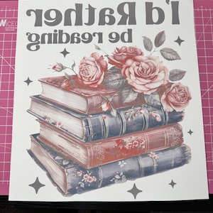 K&ouml;nnte beinhalten: Ein wei&szlig;er Hintergrund mit dem Text "I'd rather be reading" in Grau. Ein Stapel Vintage-B&uuml;cher mit Blumendesigns ist mit rosa Rosen und gr&uuml;nen Bl&auml;ttern verziert. Das Bild ist mit grauen Sternen akzentuiert.