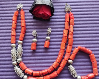 May include: A coral necklace, bracelet, and earrings set. The necklace is made of two strands of orange coral beads with silver spacers. The bracelet is made of one strand of orange coral beads with a silver clasp. The earrings are made of orange coral beads with silver hooks.