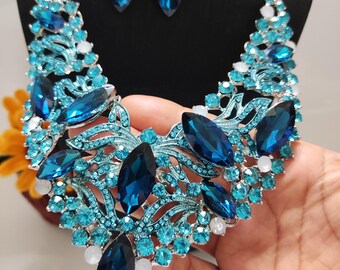 May include: A dazzling necklace and earring set featuring a vibrant combination of blue and turquoise gemstones. The necklace showcases large, deep blue teardrop-shaped stones, complemented by smaller turquoise and white accents, all set in a silver-toned metal.