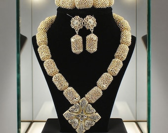 Peut inclure: Un ensemble de bijoux de couleur or exposé sur un présentoir noir dans une vitrine. L'ensemble comprend un collier avec un grand pendentif, des boucles d'oreilles assorties et un bracelet. Le collier et le bracelet présentent un motif tissé, tandis que le pendentif et les boucles d'oreilles ont des détails complexes.