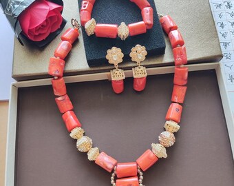 May include: A coral jewelry set with a necklace, bracelet, and earrings. The set is made of red coral beads and gold accents. The necklace has a pendant with a large coral bead.