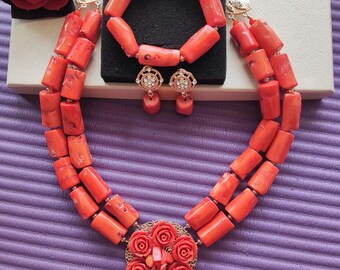 May include: A coral jewelry set with a necklace, bracelet, and earrings. The necklace is a double strand of coral beads with a large floral pendant. The bracelet is a single strand of coral beads. The earrings are small coral beads with gold accents.
