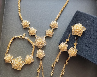 May include: A gold-tone jewelry set with a necklace, bracelet, and earrings. The set features intricate floral designs with delicate chains and dangling accents.