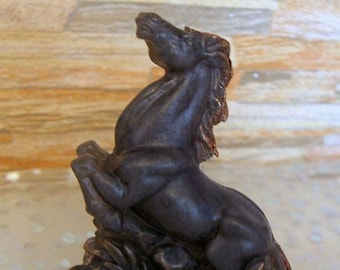 Könnte beinhalten: Dunkelbraune Pferdestatue, die sich auf den Hinterbeinen aufbäumt, mit detaillierter Mähne und Schweif. Die Skulptur hat eine bronzefarbene Verzierung und steht auf einem felsigen Sockel, der eine dynamische Pose zeigt.