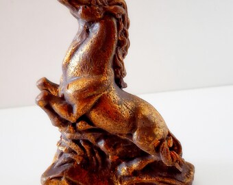 Könnte beinhalten: Bronzefarbene Pferdestatue, die sich auf ihren Hinterbeinen aufbäumt, auf einem strukturierten Sockel. Die Skulptur hat eine metallische Oberfläche mit goldenen Akzenten, die das Licht einfangen. Diese dekorative Figur ist ein klassisches Wohnaccessoire mit Pferdemotiv.