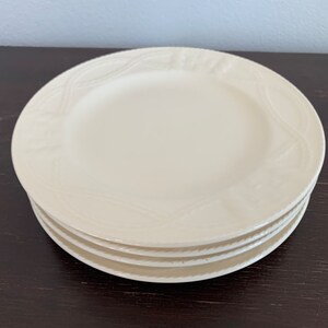 May include: A stack of four white ceramic plates with a raised, embossed design around the edge.