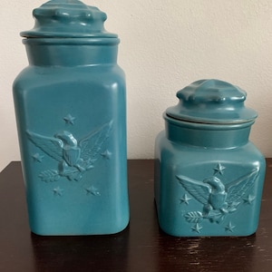 Può includere: Due barattoli in ceramica blu con coperchi. Entrambi i barattoli presentano un design di aquila in rilievo con stelle. Il barattolo più grande è più alto del più piccolo.