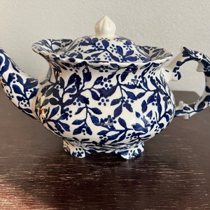 Op de afbeelding: Een witte theepot met een blauw bloemenpatroon. De theepot heeft een deksel en een handvat.