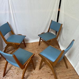 May include: Four mid-century modern chairs with light blue seats and wooden frames. The chairs have a unique, angled design, with the seat and backrest appearing to float within the frame. The chairs are arranged in a circular pattern.