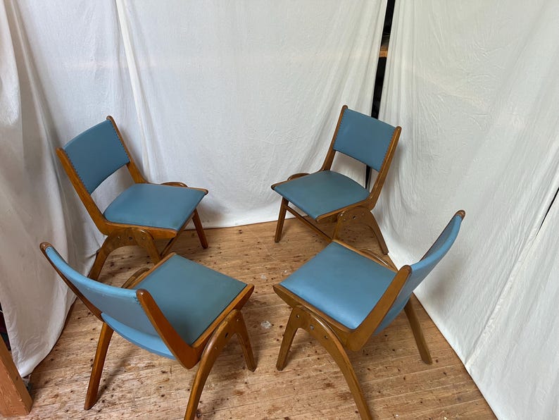 May include: Four mid-century modern chairs with light blue seats and wooden frames. The chairs have a unique, angled design, with the seat and backrest appearing to float within the frame. The chairs are arranged in a circular pattern.
