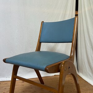 May include: A mid-century modern chair with a light blue seat and back. The chair has a wooden frame with a curved back and legs. The seat and back are upholstered in a smooth, solid-coloured material.