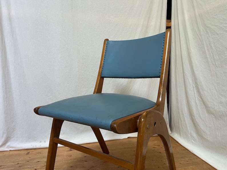 May include: A mid-century modern chair with a light blue seat and back. The chair has a wooden frame with a curved back and legs. The seat and back are upholstered in a smooth, solid-coloured material.