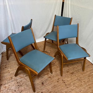 May include: A collection of four mid-century chairs. Each chair has a light blue seat and back, with a wooden frame. The chairs have a distinctive, curved design and are on a wooden floor.