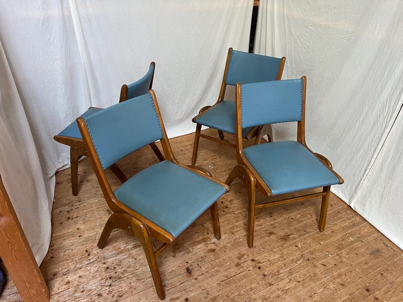 May include: A collection of four mid-century chairs. Each chair has a light blue seat and back, with a wooden frame. The chairs have a distinctive, curved design and are on a wooden floor.