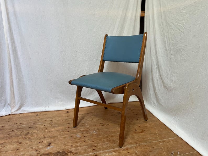 May include: A mid-century modern chair with a light blue seat and backrest. The chair has a wooden frame with a curved back and legs. The seat and back are upholstered in a smooth, solid-coloured material. The chair is set against a white backdrop.