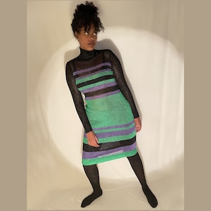 May include: A woman wearing a green, black, and purple striped long-sleeved dress with a turtleneck.