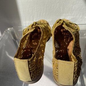 May include: A pair of gold-colored, open-weave shoes with matching laces. The shoes have a rounded toe and a low, flat sole. The material appears to be a metallic thread or yarn, creating a shimmering effect. The shoes are likely for casual wear.