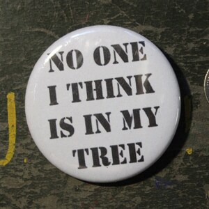 May include: A circular white pinback button featuring the black text NO ONE I THINK IS IN MY TREE, positioned next to a United States quarter coin for scale, which has a diameter of approximately 0.955 inches, providing a clear size reference.