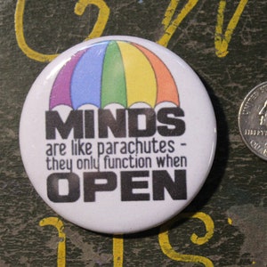 以下が含まれることがあります： 虹色の傘のデザインと「MINDS are like parachutes - they only function when OPEN」というテキストが書かれた白いボタン。
