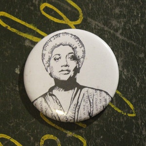 May include: A white button with a black and white image of a woman with short hair. The button has text around the edge that says "Silence is not an option".