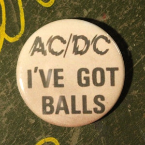 May include: A white button with black text that reads "AC/DC I'VE GOT BALLS".