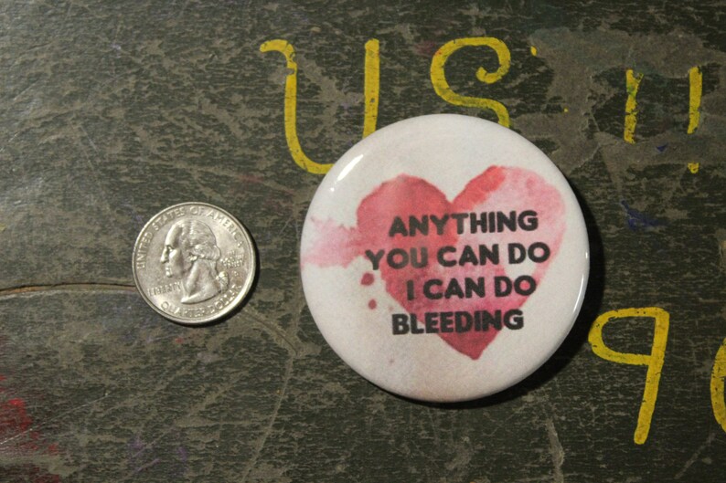 May include: A white button with a pink watercolor heart and the text "Anything you can do I can do bleeding".