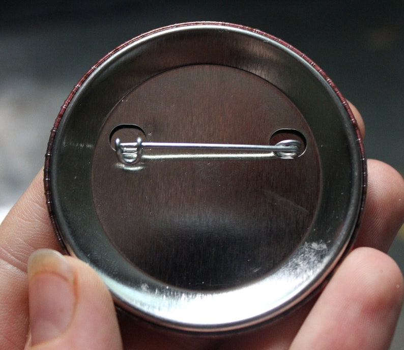May include: The back of a round button with a metal pin and a brown border.