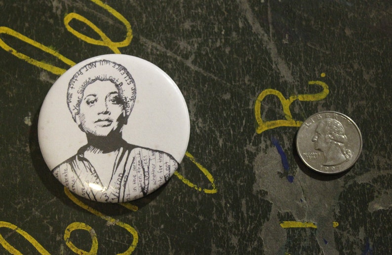 May include: A white button with a black and white image of a woman with short hair. The button has text around the edge that says "Silence is not an option".