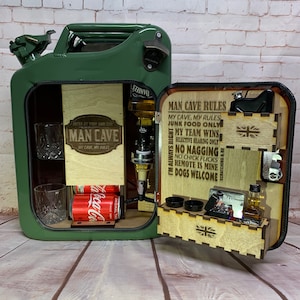 May include: A green metal repurposed gas can bar with a wooden interior. The bar features a bottle opener, a liquor dispenser, two cans of soda, a shot glass, and a small wooden shelf with a sign that reads "Man Cave Rules". The rules include "Junk Food Only", "My Team Wins", "Selective Hearing Only", "No Nagging", "No Chick Flicks", "Remote is Mine", and "Dogs Welcome".