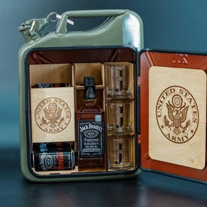 May include: A green metal Jerry can converted into a bar cabinet. The interior features wooden compartments holding a Jack Daniel's whiskey bottle, shot glasses, and Coca-Cola cans. The cabinet doors display the United States Army emblem.