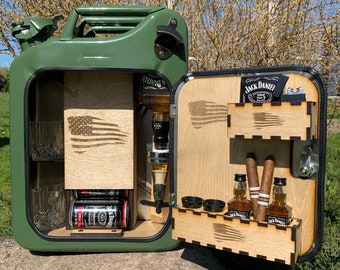 Puede incluir: Un bar de metal verde en forma de bidón de gasolina con un interior de madera. El bar tiene un abridor de botellas incorporado, un estante para vasos, un porta botellas y un pequeño estante para aperitivos. La puerta está abierta, revelando un estante con dos botellas de Jack Daniel's, dos cigarros y un pequeño estante para vasos de chupito. El bar está sentado en una gran roca.