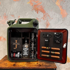 Peut inclure: Un bidon Jerry vert transformé en bar. L'intérieur comprend une bouteille de whisky Jack Daniel's, des verres à shot, une canette de Coca-Cola et une boîte en bois avec le texte "JailCrafting". La porte contient des cigares et des accessoires.