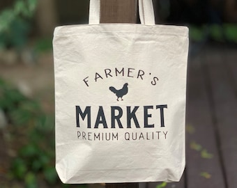 May include: A white canvas tote bag with black text that reads "Farmer's Market Premium Quality" and a black silhouette of a chicken.