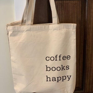 May include: A beige canvas tote bag with black text that reads "coffee books happy".
