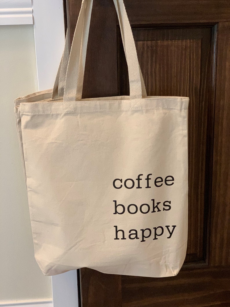 May include: A beige canvas tote bag with black text that reads "coffee books happy".